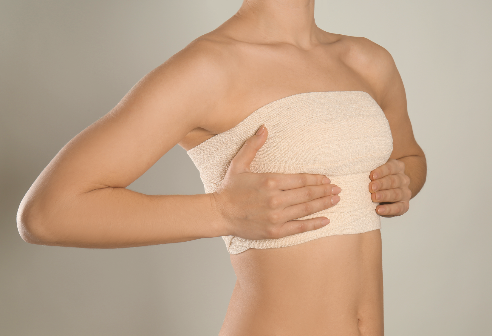 After Breast Surgery Bra: Woman with post-breast surgery compression bands gently holding her hands over her chest