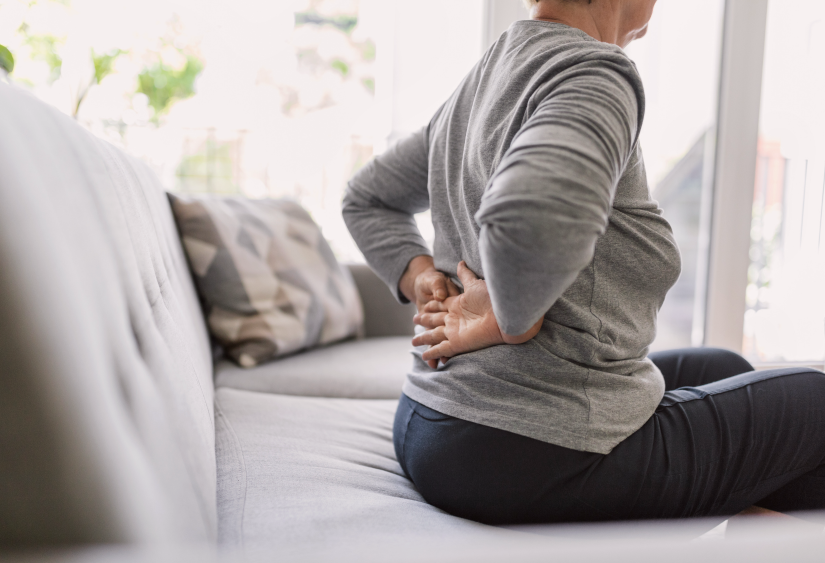 chronic pain bra: woman holding her back in pain whilst sitting