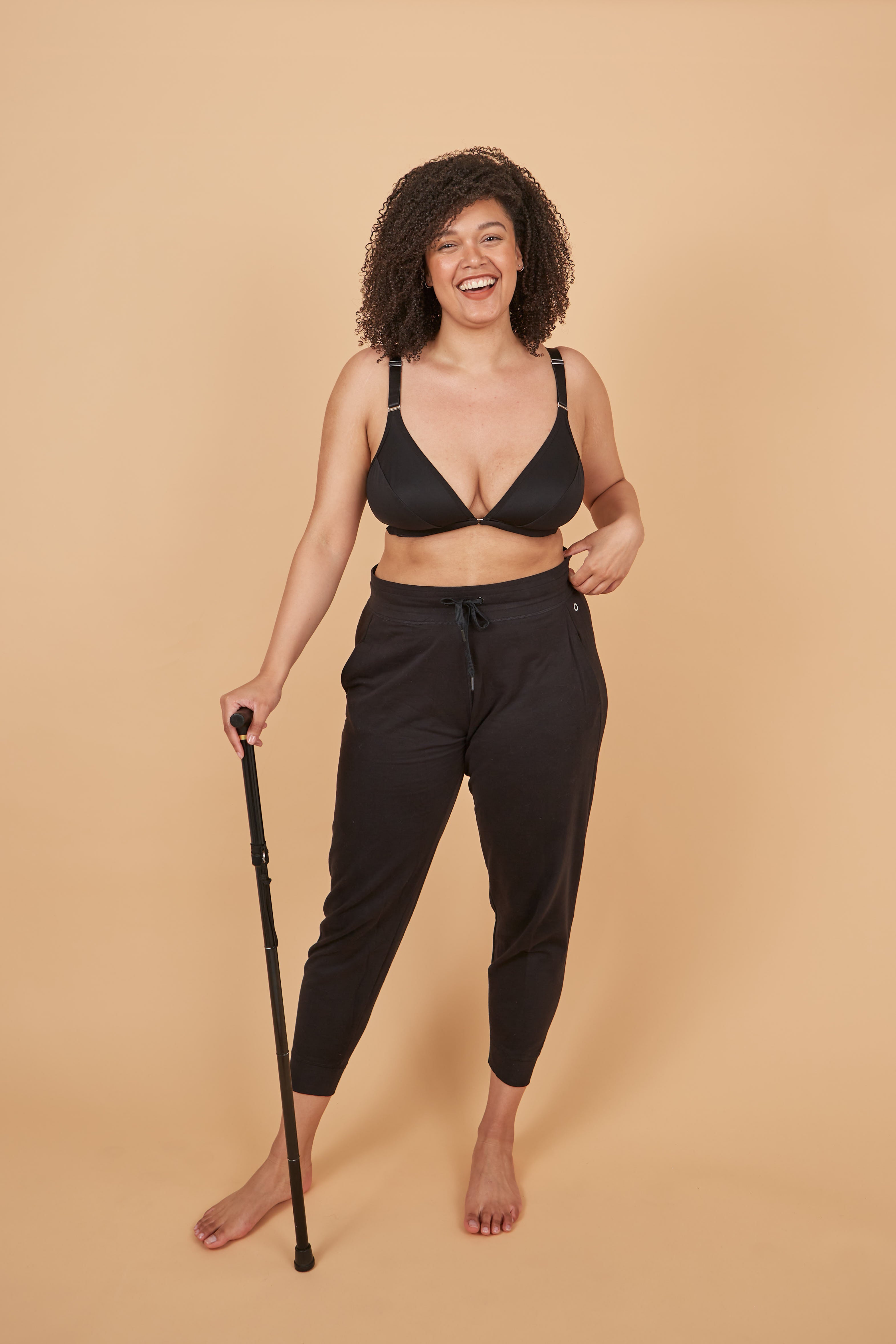 beautiful young model smiling widely at the camera while leaning on her cane and wearing the velcro front closure adaptive bra from springrose